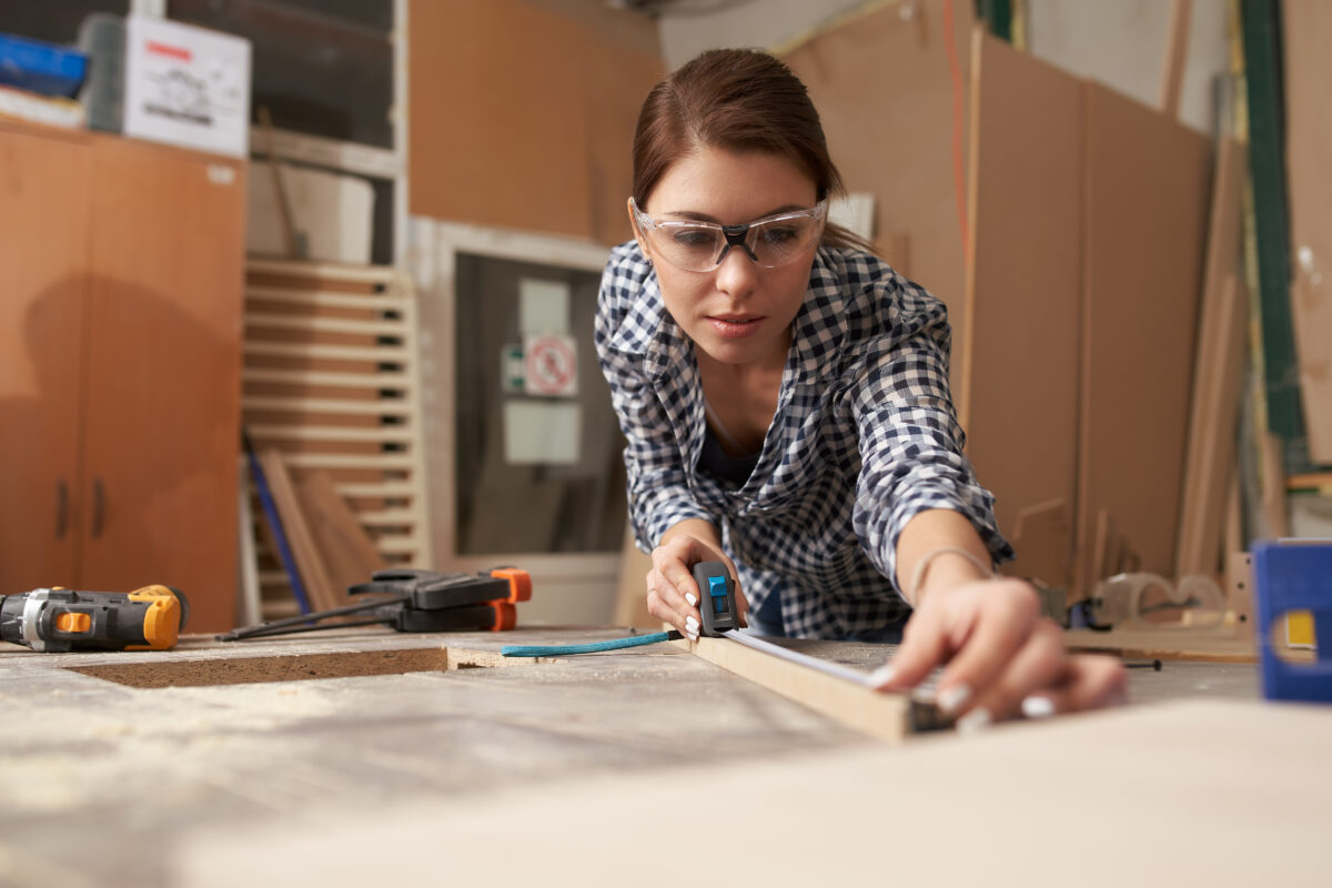 Young woman woodworker with wooden board behind workbench Bespoke